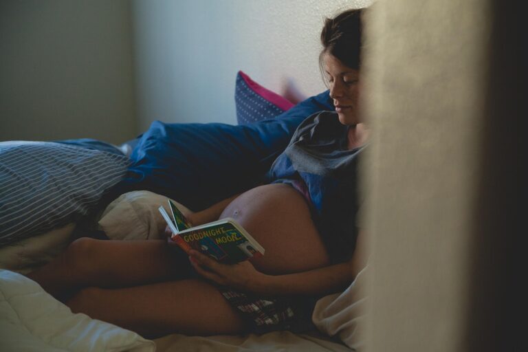 Gestante sorridente lendo um livro próximo à barriga em um ambiente acolhedor